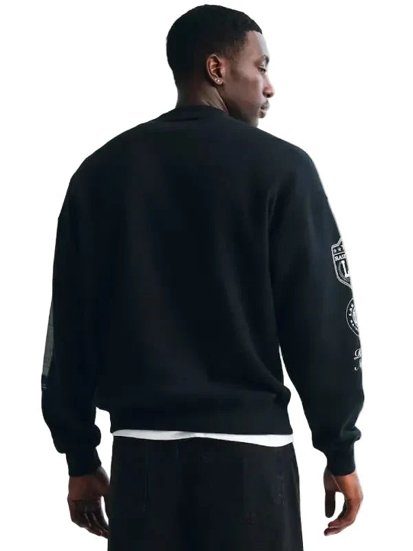 A man wearing a black crewneck sweatshirt with white graphic prints on the sleeves, shown from the back against a plain light background.