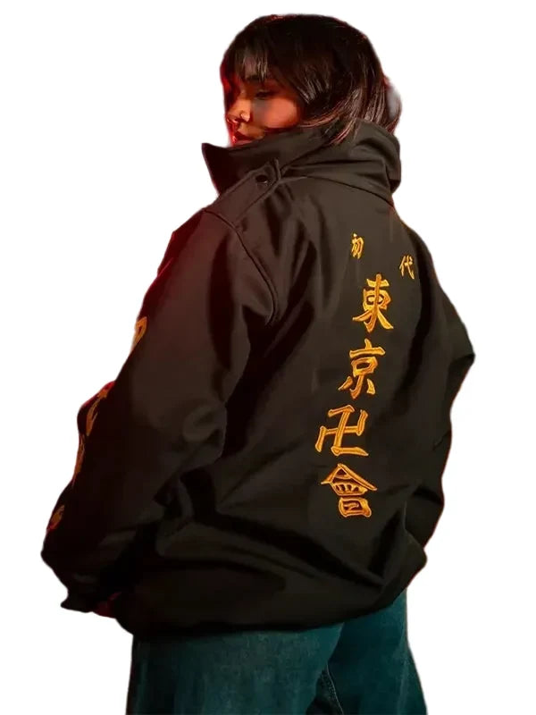 A person standing on a city street at night wearing an oversized black jacket with large gold Japanese characters printed down the back, paired with blue jeans.