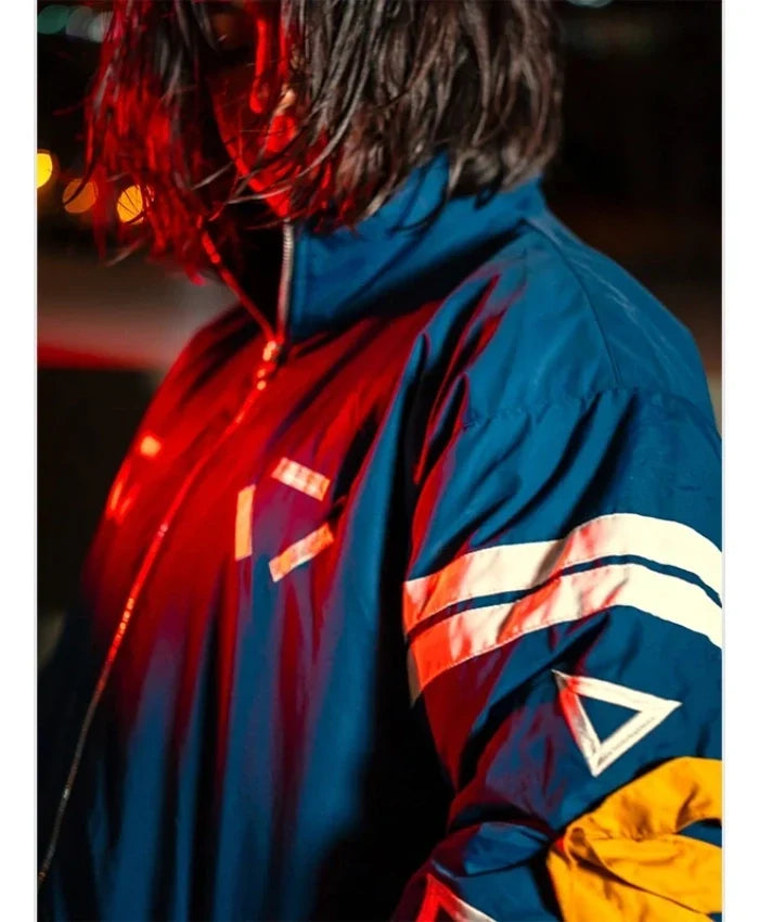 A close-up side view of a person wearing a reflective blue jacket with white stripe details and a yellow panel on the lower arm, under dramatic red and blue lighting.