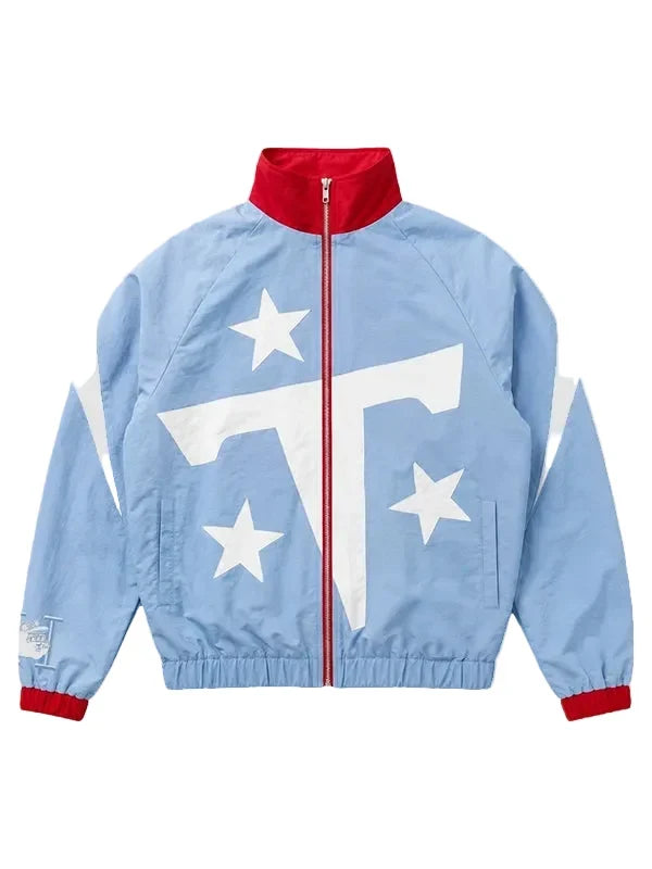 A light blue windbreaker jacket featuring a bold white graphic on the front with three white stars and a large white letter 'T', accented by a red collar, red zipper, and red cuffs.