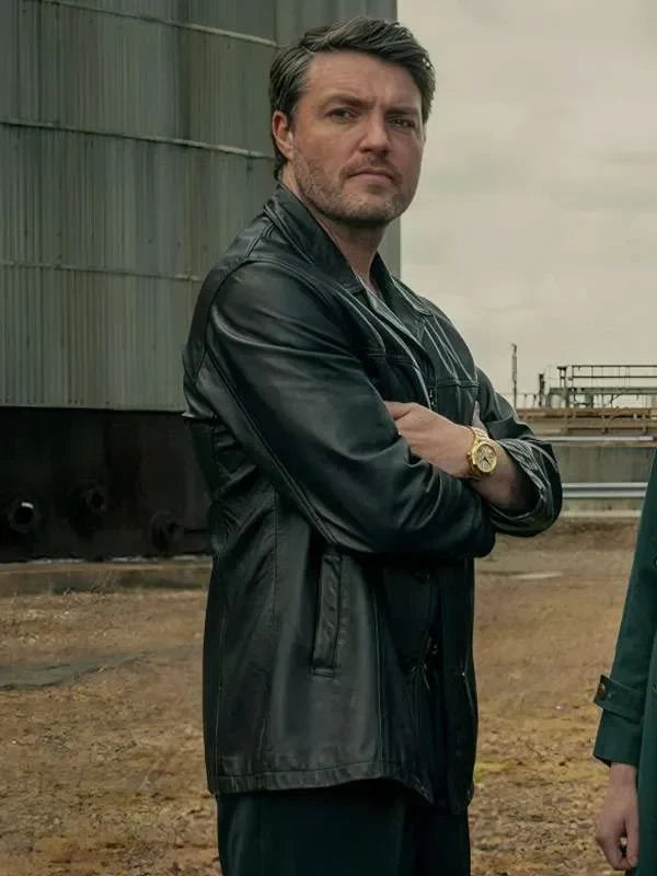 Man wearing a dark jacket standing outdoors with a cloudy sky.