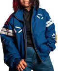 A person wearing a blue oversized zip-up jacket with white geometric stripe graphics on the chest and sleeves, layered over a black top and blue jeans, against a plain white background.
